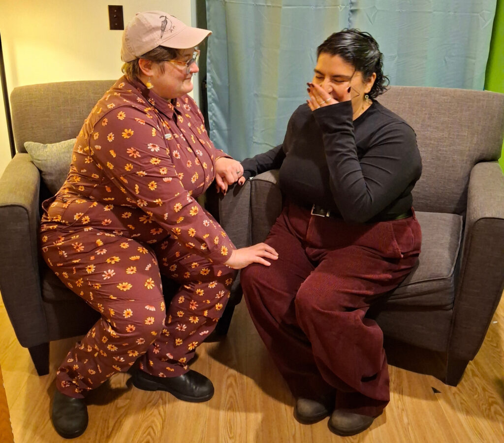 a couple sit in comfortable chairs at a fertility consultation appointment. One member of the couple looks overwhelmed with emotion
